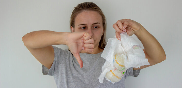A woman's hand holding two disposable baby diapers against a light background