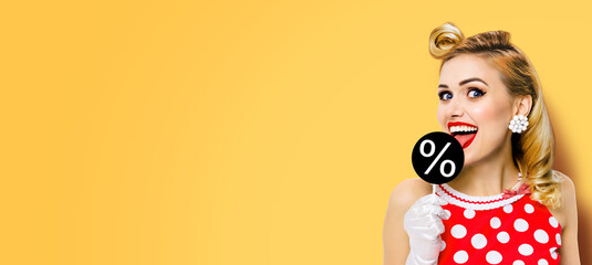 Black Friday ad. Very tasty price discount, sale concept image. Happy cute beautiful woman licking signboard with % precentage sign, in pinup red dress, isolated orange yellow background. Wide banner