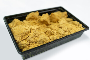 A tray of soft and jelly-like warabi mochi coated generously with golden kinako.The warabi mochi pieces have a tender, slightly translucent texture underneath the powder on the black plastic container