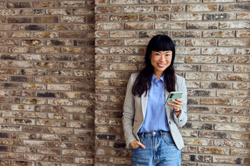 Asian Woman in Blazer With Smartphone Against Brick Wall &ndash; Casual Business Portrait