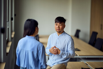 Obraz premium Asian Man and Woman Having a Professional Conversation in a Modern Office Workspace