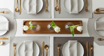 An overhead flat lay shot showcases a modern and elegant dining table setting. A long, rectangular wooden tray serves as the centerpiece, holding three small glass vases, each with a single white