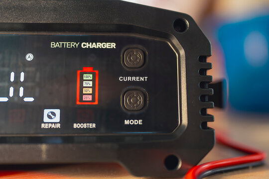 Close-up of digital battery charger screen showing charging levels from 25% to 100% with current and mode buttons. Concept of automotive power, energy efficiency, and battery maintenance.