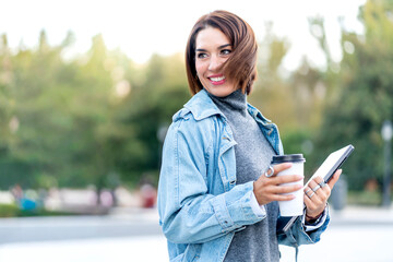 Smiling woman walking in city holding coffee and tablet