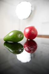 A fresh green avocado and a red garnet lies on a glass kitchen stove