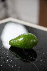 A fresh green avocado lies on a glass kitchen stove