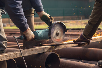 Workers' hands with an electric grinder cut metal at a construction site. Men at work.