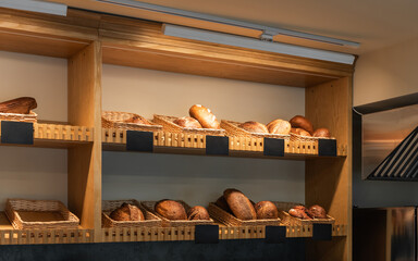Artisanal bread display in modern bakery. Bread loaves displayed in wicker baskets on wooden shelves in a bakery. Several blank black labels are visible for pricing.