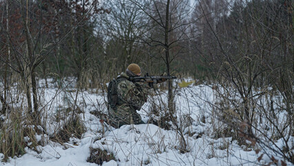Soldier on a military mission in the wilderness. Forest full of snow at winter. Hiding in the snow and aiming. War tactics