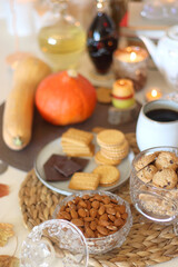 Lit candles, cookies, chocolate, nuts, tea, wine, pumpkins, books, reading glasses and autumn leaves on the table. Autumnal hygge at home. Selective focus.
