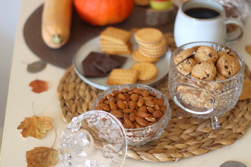 Lit candles, cookies, chocolate, nuts, tea, wine, pumpkins, books, reading glasses and autumn leaves on the table. Autumnal hygge at home. Selective focus.
