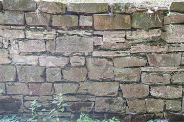 Ancient, Central European village, rustic stone wall, weathered, worn, irregularly shaped stones, old structure, erosion, damage, cracks, crevices, moss, greenery, earthy tones grey, brown, green,. a