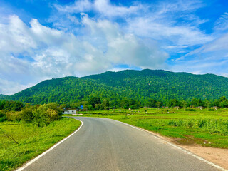 Scenic road leading to lush green mountain under a blue sky with clouds a peaceful landscape for travel and nature themes on a sunny day