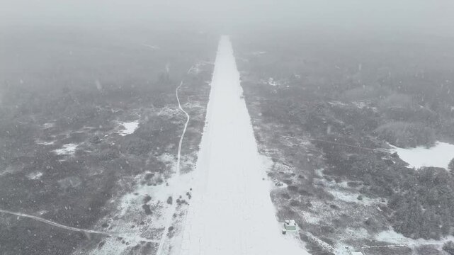 Slow motion raising vertically above the snowy, empty runway at the decommissioned Killaloe/Bonnechere Airport in Ontario, Canada, during heavy winter snowfall