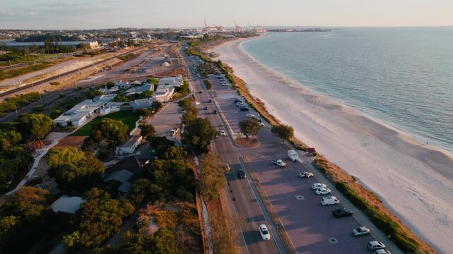 Aerial view of a road runs parallel to the beach with parked cars, palm trees, and the ocean visible during a beautiful sunset in Perth, Australia