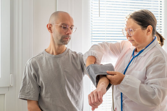 female doctor measuring blood pressure of male patient, using digital monitor, routine healthcare visit, medical examination, health screening for patient well-being, professional care with trust