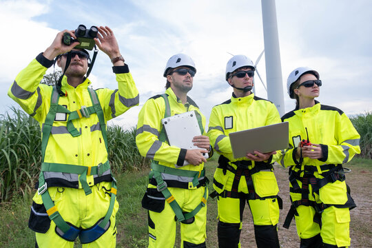 Wind farm technicians analyze data and assess equipment while conducting site inspections on a cloudy day