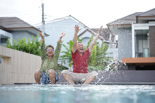 Happy senior couple splashing water and having fun by the pool, Joyful elderly couple enjoying playful moments at the poolside, Active senior lifestyle with cheerful couple playing in the water
