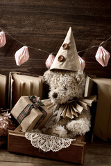 Vintage style teddy bear in paper ruff collar and a cap holding a gift box in sepia color