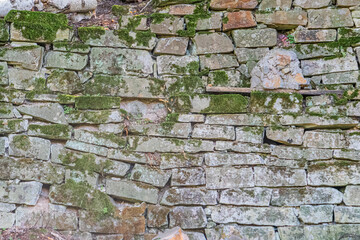 Close-up of aged Central European stone wall, irregularly shaped and colored gray limestone or similar rock, moss growth, slight curve or bulge, diffuse lighting, multi-layered perspective, realistic