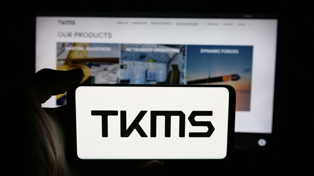 Stuttgart, Germany - 11-20-2025: Person holding cellphone with logo of company ThyssenKrupp Marine Systems (TKMS) on screen in front of webpage. Focus on phone display.
