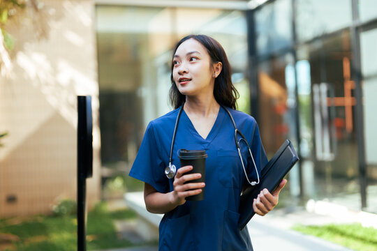 Asian healthcare worker walking with coffee and folder - Powered by Adobe