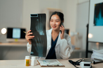 Asian doctor examining x-ray discussing treatment on phone