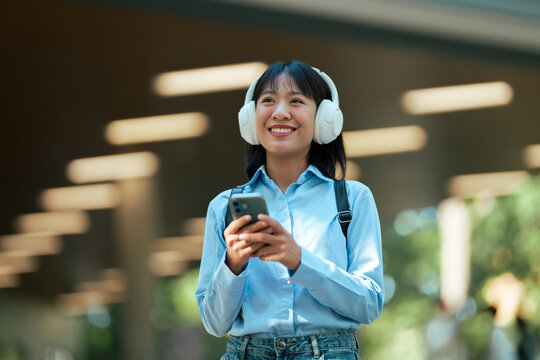 Asian woman listening music on headphones holding smartphone