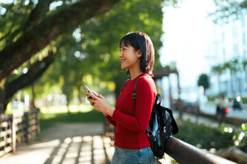 Asian woman smiling using smartphone in park