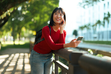 Young Asian woman smiling using smartphone outdoors