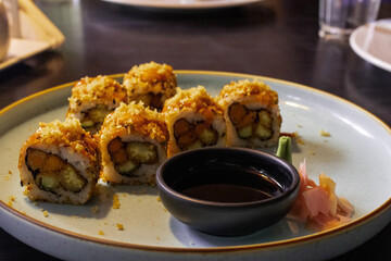 Gourmet plate of crispy tempura vegetable maki sushi rolls with condiments in a moody restaurant setting