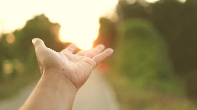 Hand reaching toward warm sunset light on a rural path, Hope concept, A hand reaching the glowing sunset, creating a warm, dreamy atmosphere with soft focus and natural light - Powered by Adobe