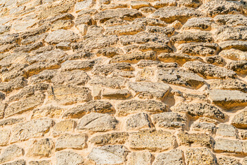 Close-up of an ancient Central European stone village wall, with irregularly shaped, aged stones, showing color and texture variations Partial sunlight creates contrasting shadows No objects or peo