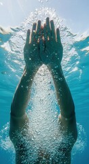 Close-up of a person's hands rising through clear blue water toward sunlit surface creating dynamic bubbles