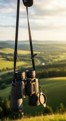 Binoculars hanging suspended against a vast green landscape illuminated by golden sunlight for adventure and discovery