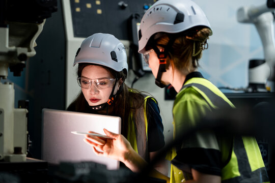 Two women wearing yellow and white safety gear are looking at a device
