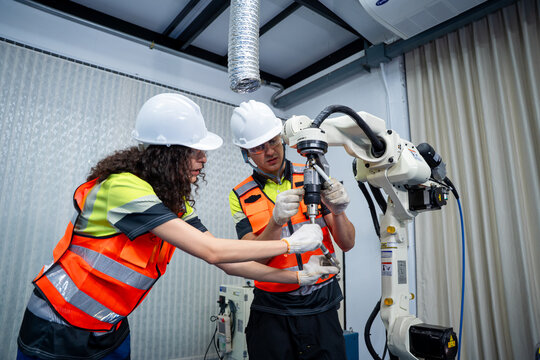 Two people in orange vests are working on a robot