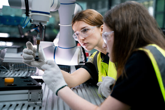 Two women wearing safety goggles and gloves are working on a machine