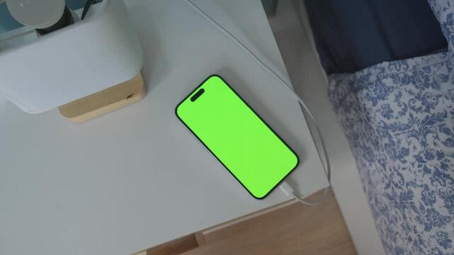Top view smartphone charging on nightstand with green screen