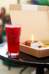 Iced Red Fruit Beverage on Outdoor Table Beside Candle and Cardboard Box