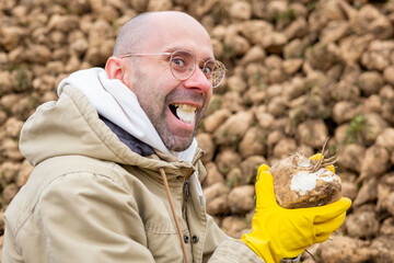 Cheerful Playful young farmer playfully biting into piece freshly harvested sugar beet, tasting crop, healthy eating, genuine smile, agricultural harvest joy, examining sweet freshness root vegetable