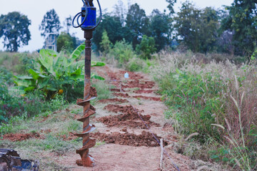 A soil auger bit with mud on a freshly dug path.