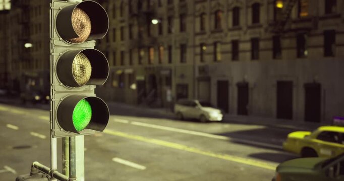 A bustling street intersection features green traffic lights with a yellow taxi waiting nearby. Buildings line the street under bright daylight, showcasing urban life.
