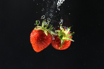 Fresh strawberries splashing in cool water against dark backdrop, a vibrant healthy treat for summer desserts and eye-catching food photography projects