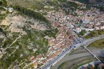 Aerial view of Berat showing hillside homes beneath the rocky slope leading to the castle and the Osum River crossing below.