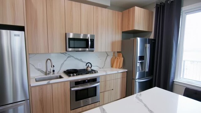 Modern kitchen featuring wooden cabinets, stainless steel appliances, marble backsplash and countertop, and window