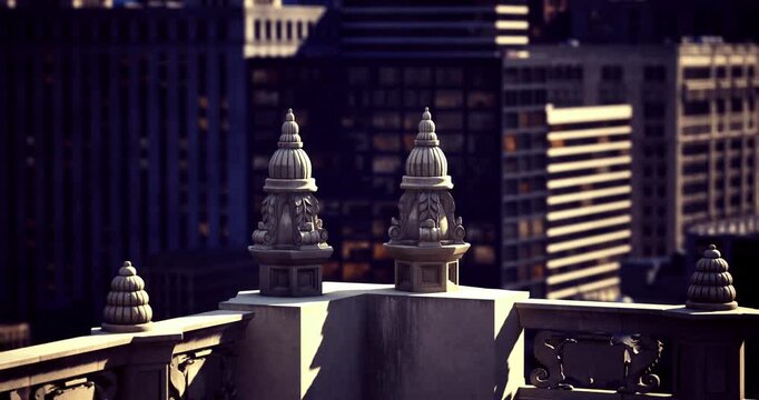 Two intricate architectural features atop a historic building overlook a vibrant city skyline during sunset. The evening light highlights the details against the backdrop of tall buildings.