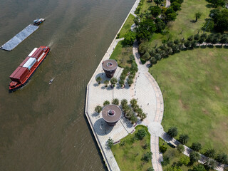 Boat is on the water near a park. The park has a walkway and a pond
