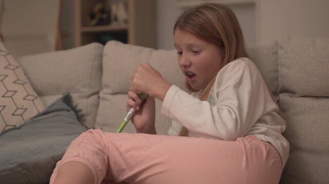 A thoughtful girl sits on the sofa at home in the evening and looks at a pen for writing