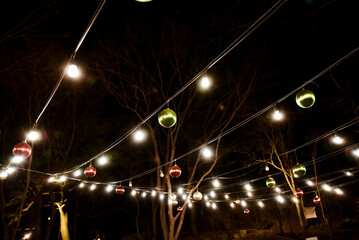 A string of Christmas lights with green and red balls hanging from the wires. The lights are lit up and the balls are glowing